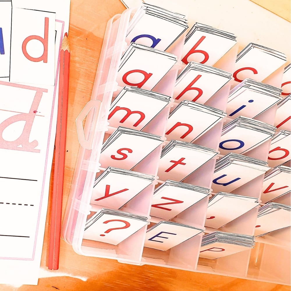 The Moveable Alphabet comes in a plastic organizer that holds flashcards with both lowercase and uppercase letters, providing excellent support for early literacy skills. Nearby are pencils and worksheet pages displaying the letter “d” in print and cursive, making the Moveable Alphabet a wonderful addition to any Montessori-inspired learning environment. Montessori Nature Printable