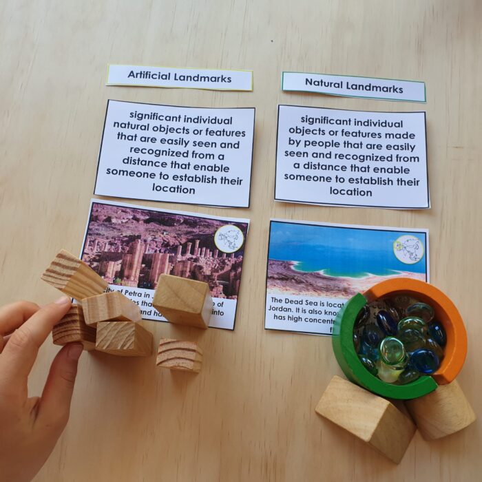 A hand arranges wooden blocks near the Landmarks in Asia Sorting Cards labeled "Artificial Landmarks" and "Natural Landmarks," each featuring a photo and description of Asian landmarks; glass marbles rest in a circular tray. Montessori Nature Printables
