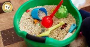 A child is engaging in a fun activity, playing with sand in a green bucket.