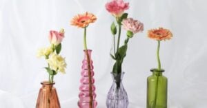 Four different flowers in pink, purple, and green glass vases are arranged in a row against a white background, creating a serene display inspired by Montessori principles. Montessori Nature Printables