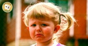 A sad little girl stands in front of a fence, showcasing her emotions.