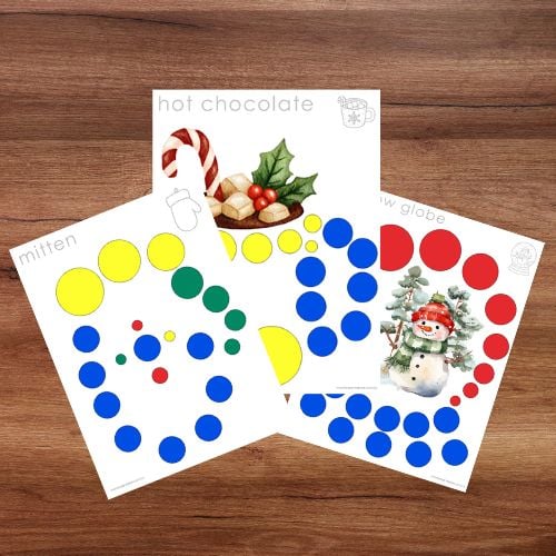 Three printable Knobless Cylinder Extension Cards: Winter Patterns shown on a wooden surface, each featuring colored dots and winter-themed images—a mitten, hot chocolate, and a snow globe—perfect for Montessori-inspired learning. Montessori Nature Printables