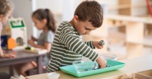 A young boy is playing with a tray in a Montessori classroom.